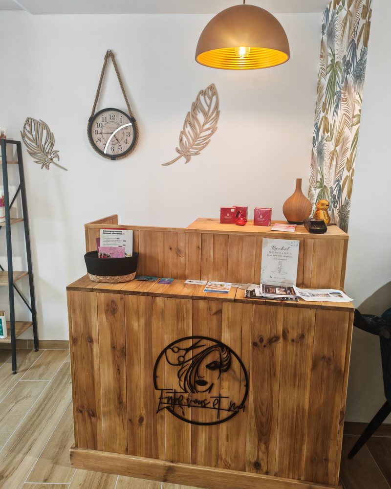 L'accueil du salon Entre Vous et Moi à Plancoët : comptoir en bois gravé au logo du salon, sous une suspension dorée
